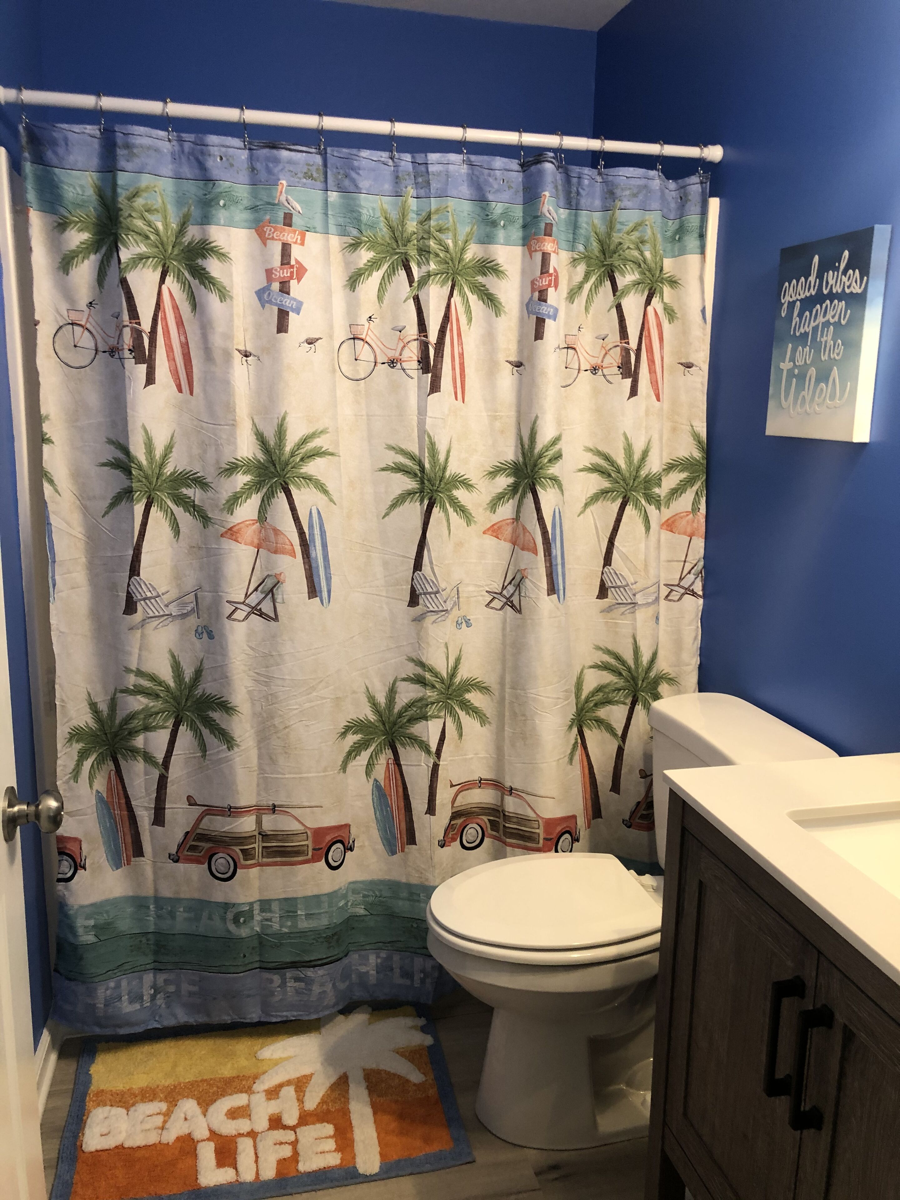 A bathroom with a beach-themed shower curtain, a toilet, and a cabinet.
