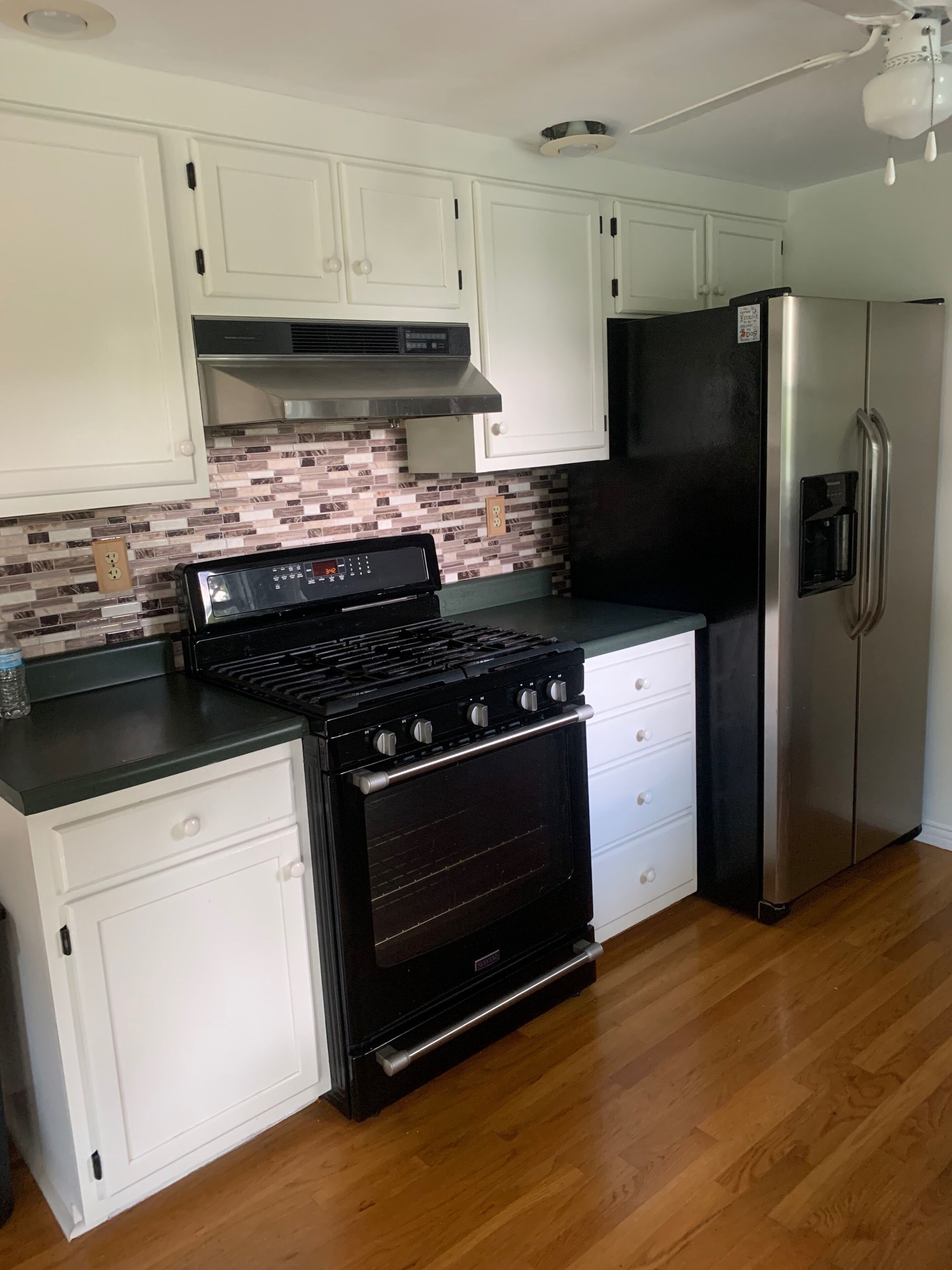 A kitchen with white cabinets, a black stove, a stainless steel refrigerator, and a tiled backsplash.