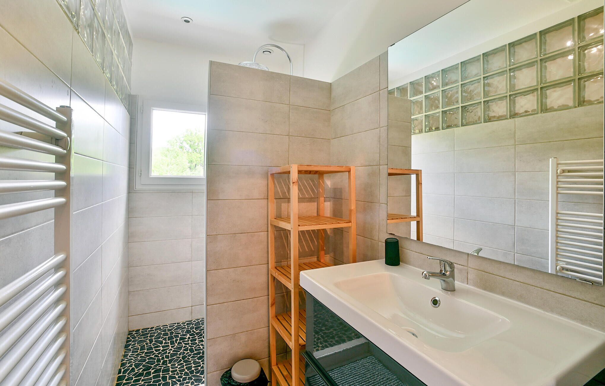 Une salle de bain avec un grand lavabo blanc, un miroir, une douche et un sol carrelé.