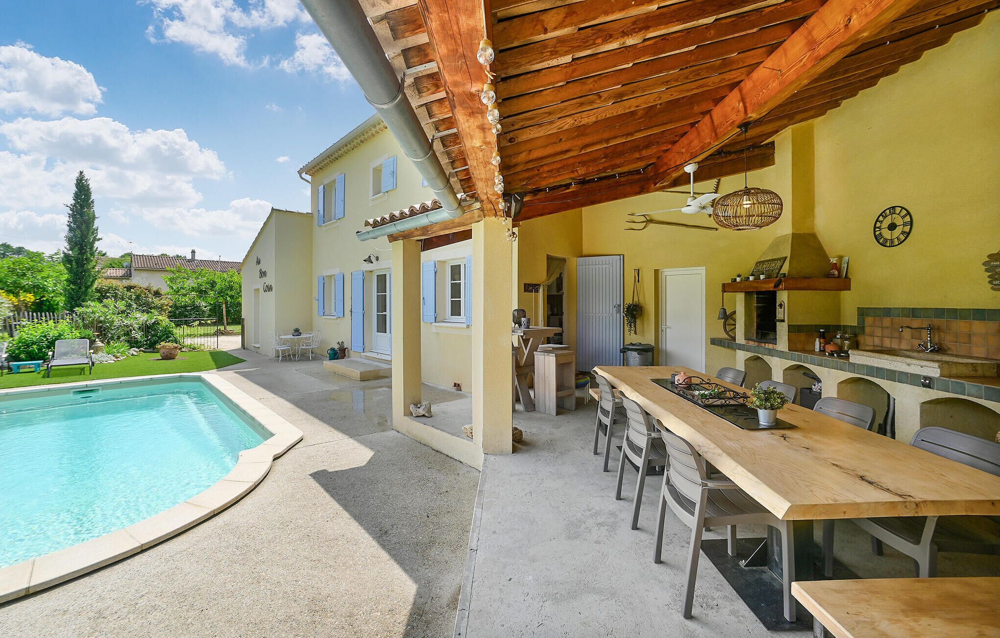 Ein Poolbereich mit einer Holzpergola, Sitzgelegenheiten im Freien und einer Küchenzeile, inklusive einer Uhr und einem Schild mit der Aufschrift 'GARDEN'.