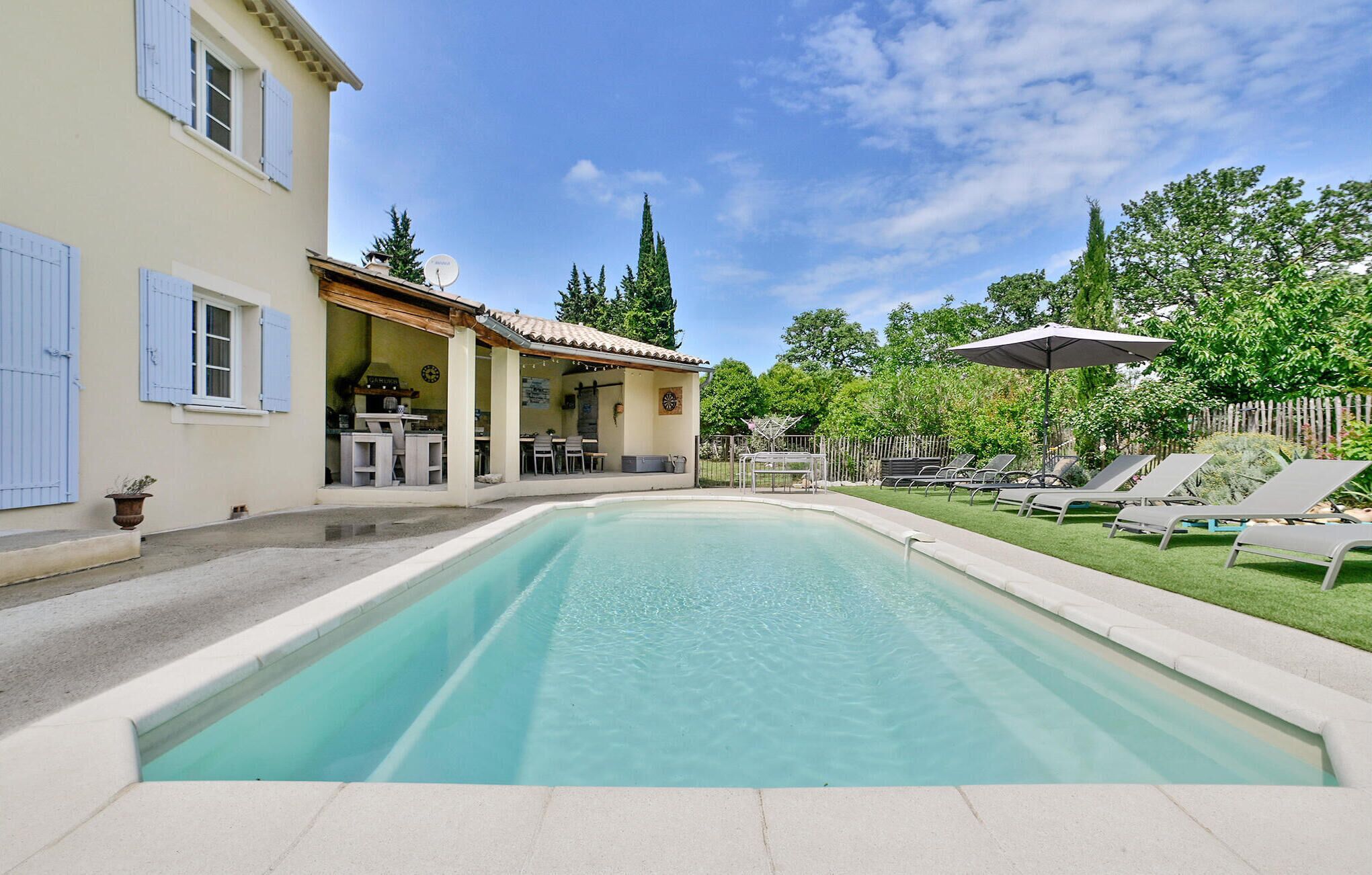 A swimming pool with a patio area, outdoor seating, and a covered structure.