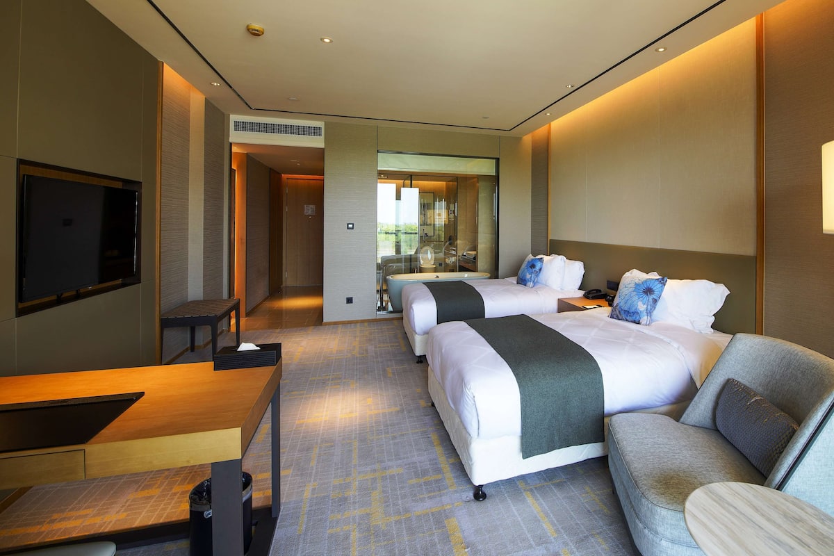 A hotel room with two beds, a desk, a TV, and a seating area.