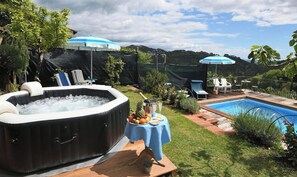 Ein Garten mit Whirlpool, Pool, Liegestühlen und Sonnenschirmen.