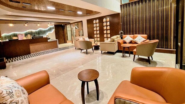 Um hall moderno com balcão de recepção, várias áreas de estar e teto alto com iluminação embutida.