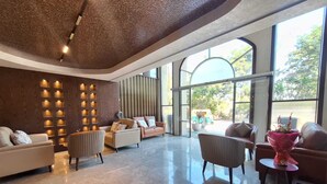 Um amplo hall com design moderno, apresentando uma área de estar com sofás e poltronas, uma parede decorativa com painéis iluminados e grandes janelas com vista para o exterior.