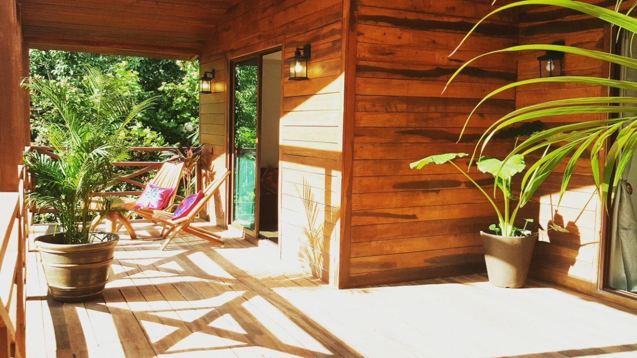 A wooden porch with a view of lush greenery, a seating area with chairs, and potted plants.