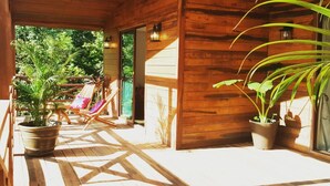 A wooden porch with a view of lush greenery, a seating area with chairs, and potted plants.