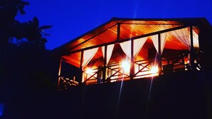 A large, open-air structure with a roof supported by beams, illuminated by warm lighting.