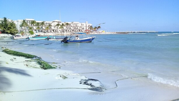 A beach with boats, a white building with arches, and a clear sky.