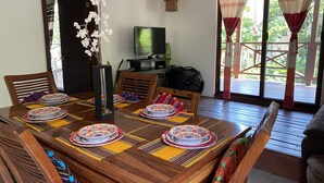 A dining area with a wooden table set for four, a television, and a view of the outdoors.
