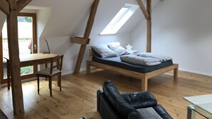 Camera soppalcata con soffitto spiovente, travi in legno, un letto, una scrivania e una sedia.