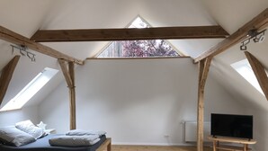 Camera mansardata con un letto, un tavolino da caffè in vetro, una televisione e travi in legno.