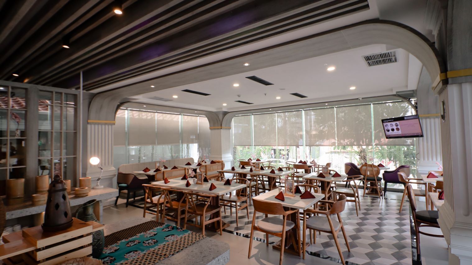 A spacious indoor dining area with multiple tables and chairs, large windows, and a modern ceiling design.