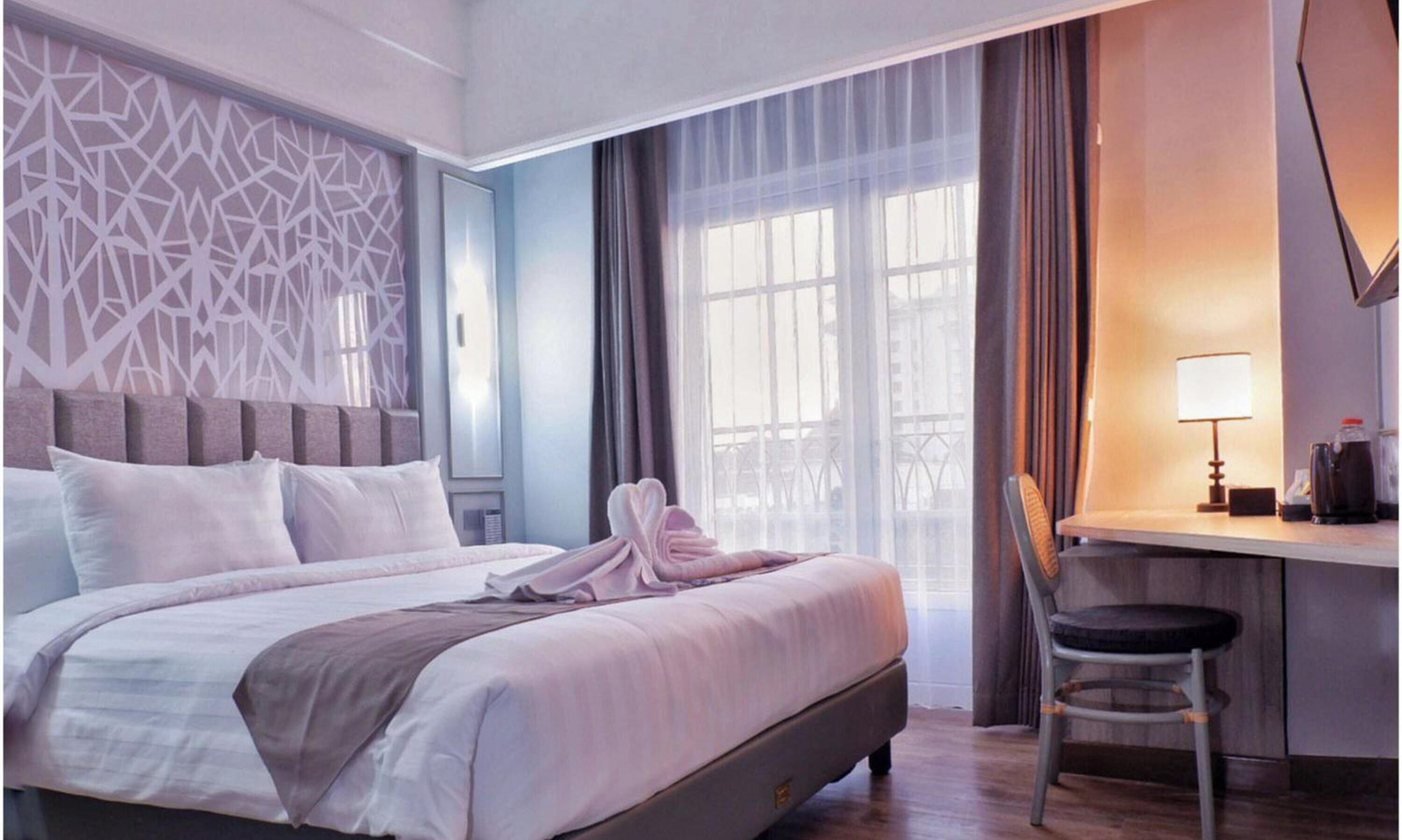 Habitación de hotel con cama, escritorio, silla y ventana con cortinas.