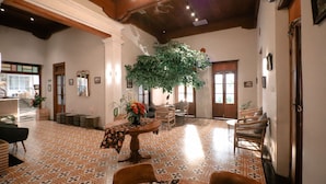 A spacious lobby with patterned flooring, a central table with a floral arrangement, and a large indoor plant. - FIM by Zigna (Surakarta)