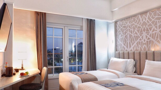 Une chambre d’hôtel avec deux lits, un bureau, une chaise et une fenêtre donnant sur le paysage urbain.