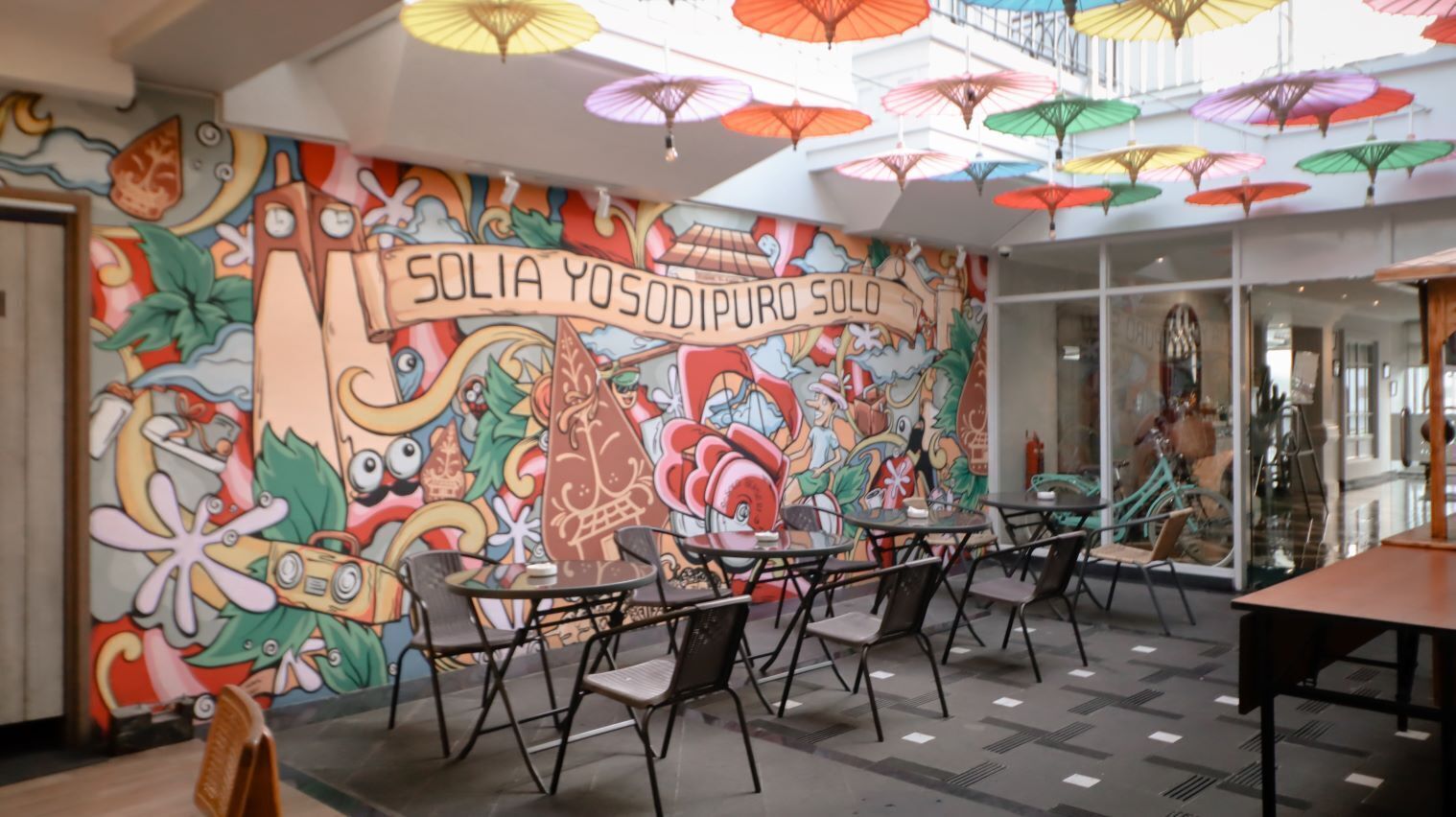 A vibrant mural with a colorful umbrella display and a café area with tables and chairs.