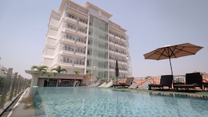 A swimming pool with lounge chairs and an umbrella, surrounded by a tall hotel building with balconies. - FIM by Zigna (Surakarta)