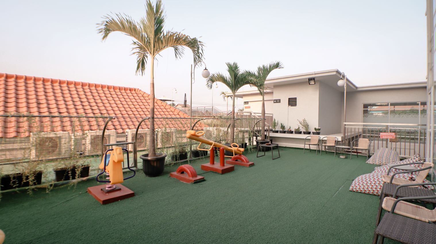 Terraza en la azotea con equipo de ejercicio, palmeras y mobiliario exterior.
