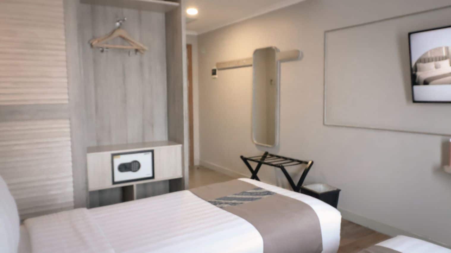 Et moderne hotelværelse med en seng, et sengebord, et knagered og et stort spejl på væggen.