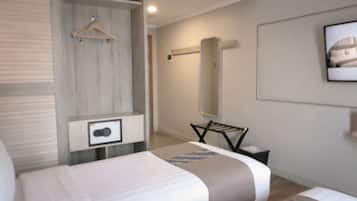 A modern hotel room with a bed, a bedside table, a hanging clothes rack, and a large mirror on the wall.