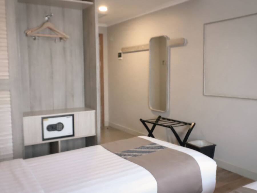 A modern hotel room with a bed, a bedside table, a hanging clothes rack, and a large mirror on the wall.