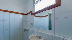 A bathroom with white tiles, a sink, a mirror, and a window. - Applewood B&B (Bogor)