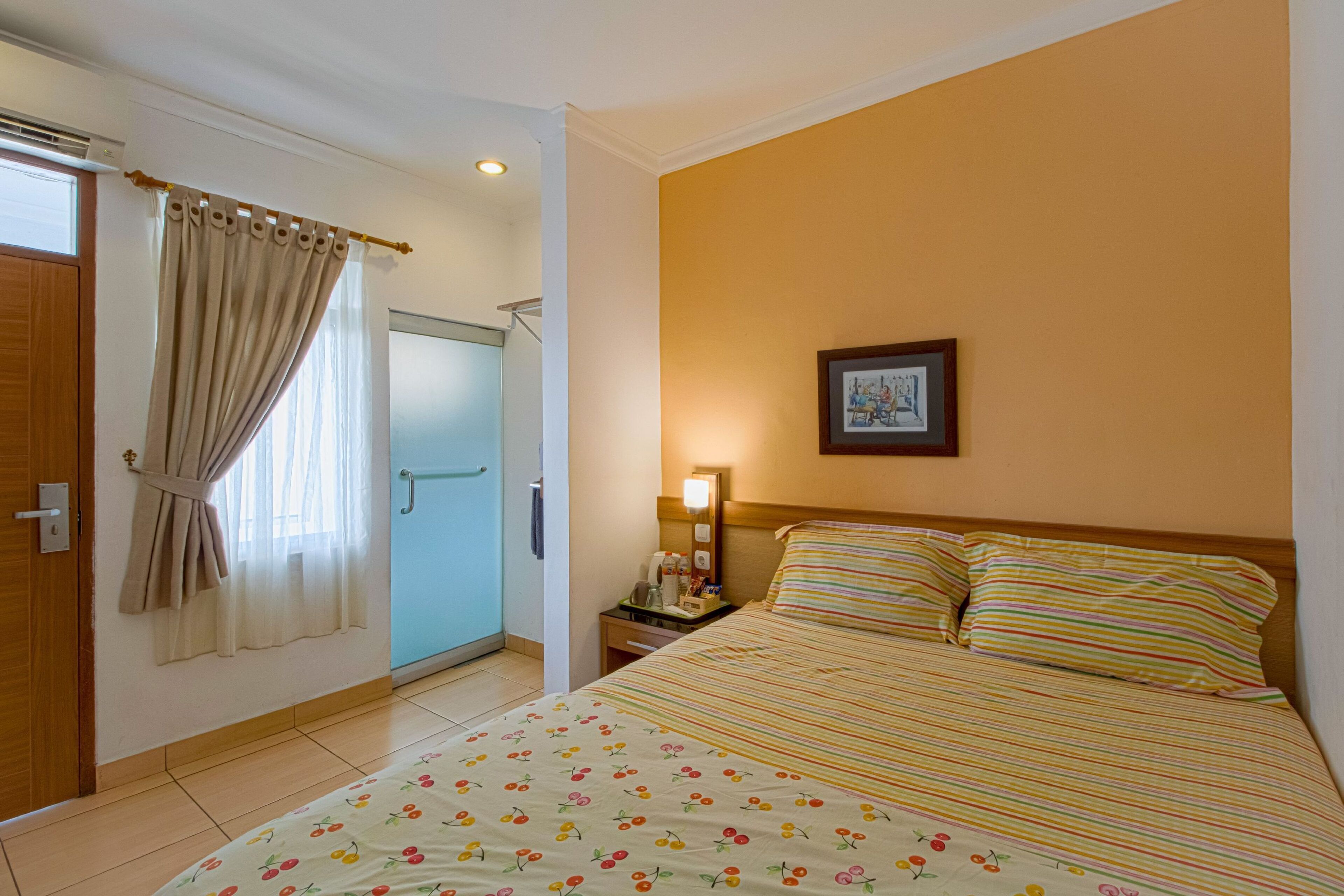 A hotel room with a bed, a nightstand, a lamp, a framed picture on the wall, and a window with curtains.