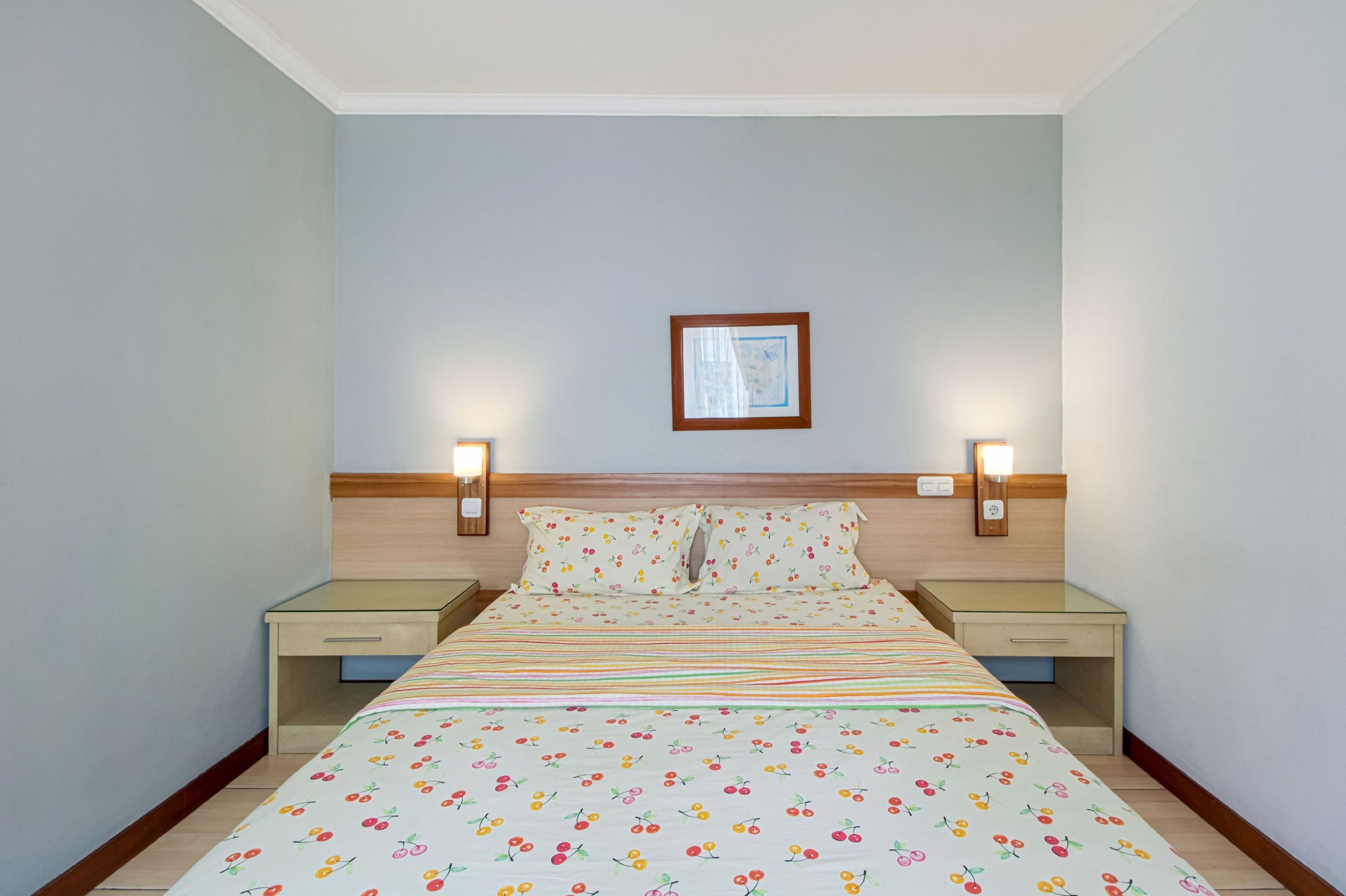 Un lit bien fait, recouvert d’une couvre-lit à motifs floraux, deux tables de chevet avec des lampes et un tableau encadré accroché au mur.
