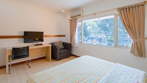 A hotel room with a bed, a desk, a chair, a television, and a window with curtains. - Applewood B&B (Bogor)