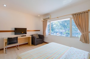 Habitación de hotel con cama, escritorio, silla, televisor y ventana con cortinas.