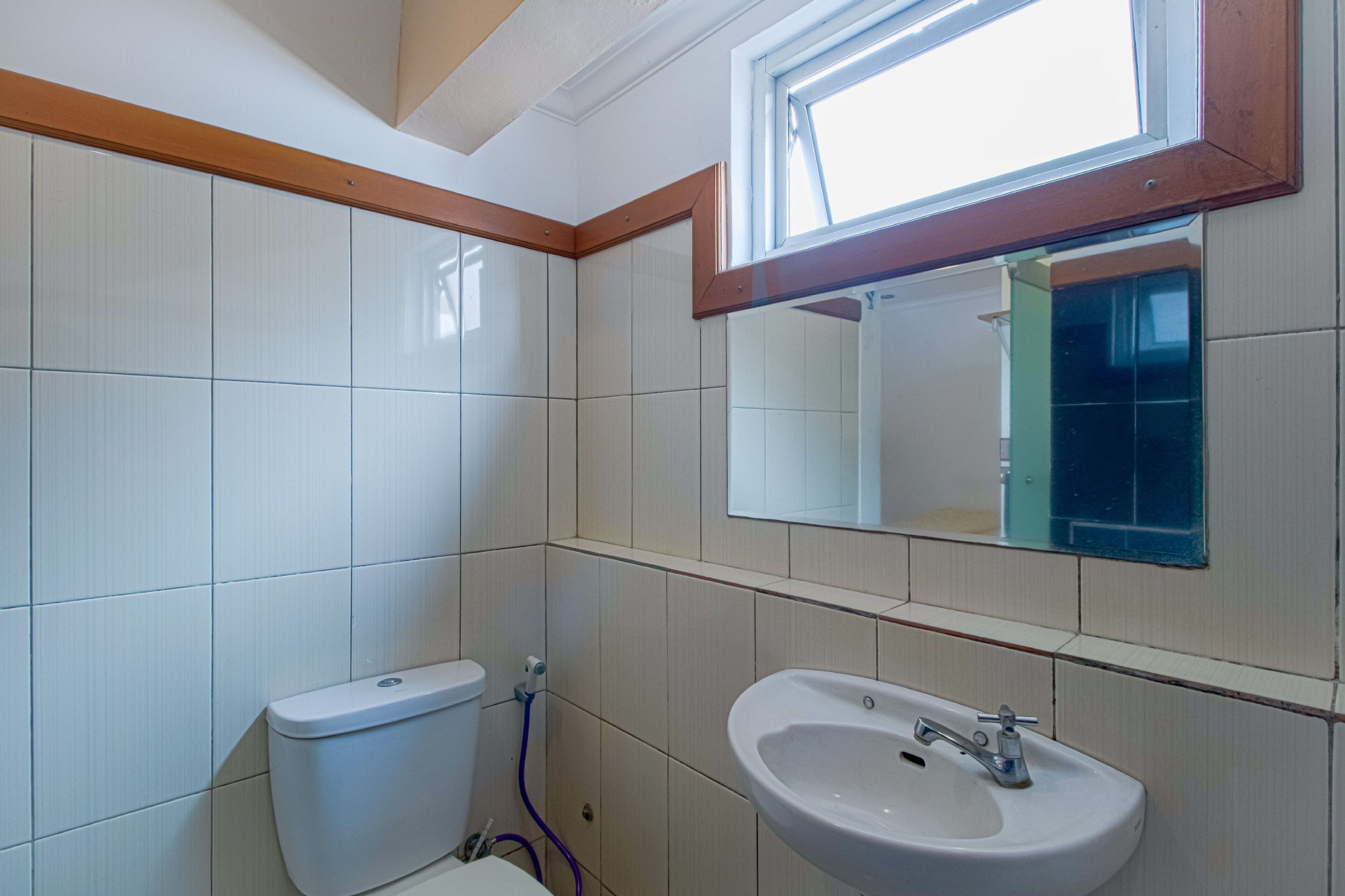 A bathroom with white tiles, a toilet, a sink, and a window above the mirror.