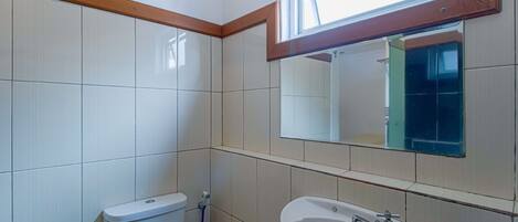 A bathroom with white tiles, a toilet, a sink, and a window above the mirror.