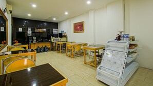 A restaurant with tables and chairs, a coffee machine, and a display case with items. - Bungur Inn Syariah (Jakarta)