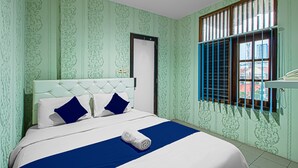 A hotel room with a bed, a window with blue shutters, and patterned wallpaper. - Bungur Inn Syariah (Jakarta)