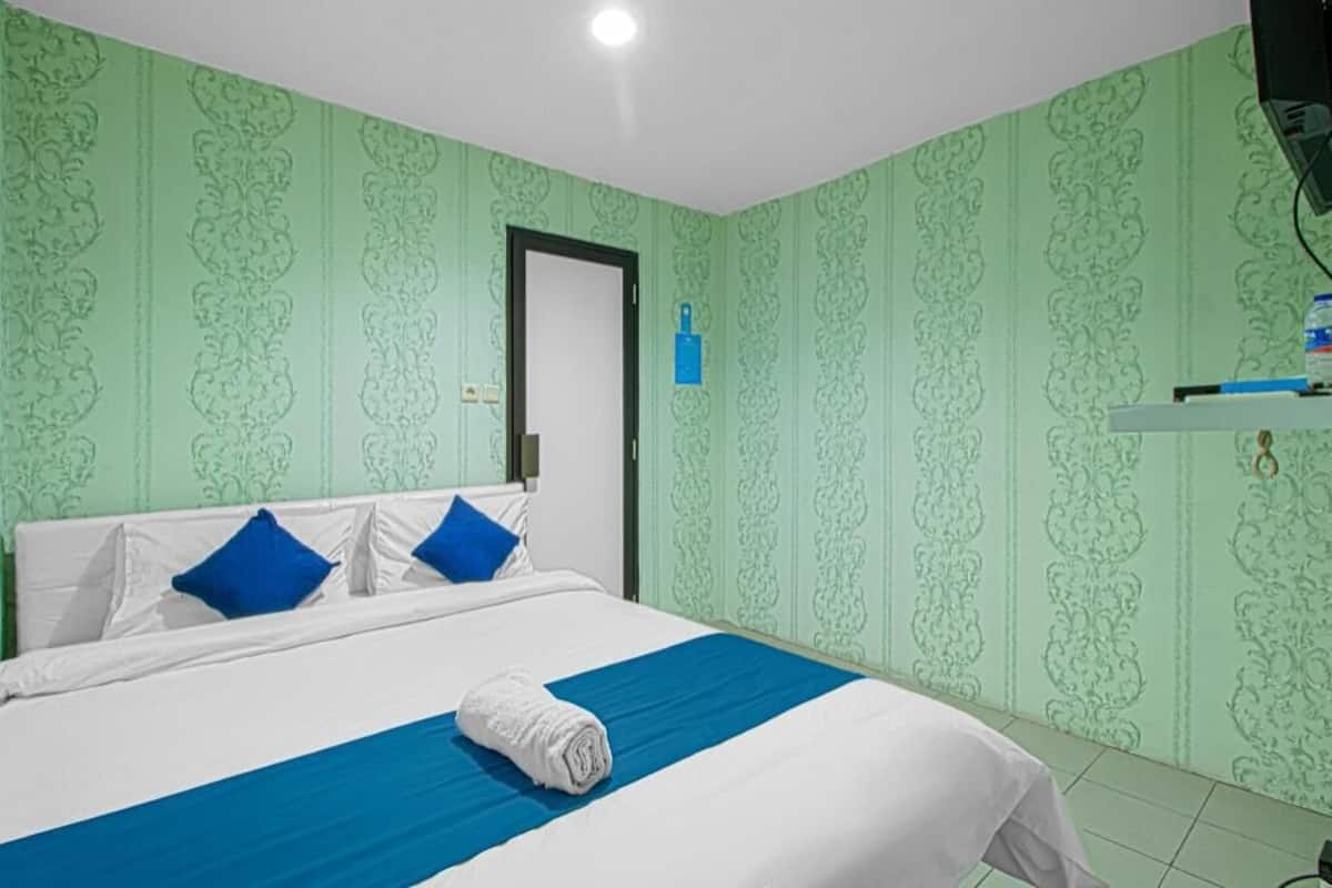 A hotel room with a bed, a door, a blue towel, and green patterned wallpaper.