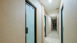 A corridor with doors, a tiled floor, and a ceiling light fixture. - Bungur Inn Syariah (Jakarta)