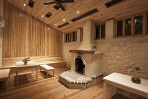 Una habitación con paredes de madera, chimenea de piedra, ventilador de techo y una mesa con un banco.