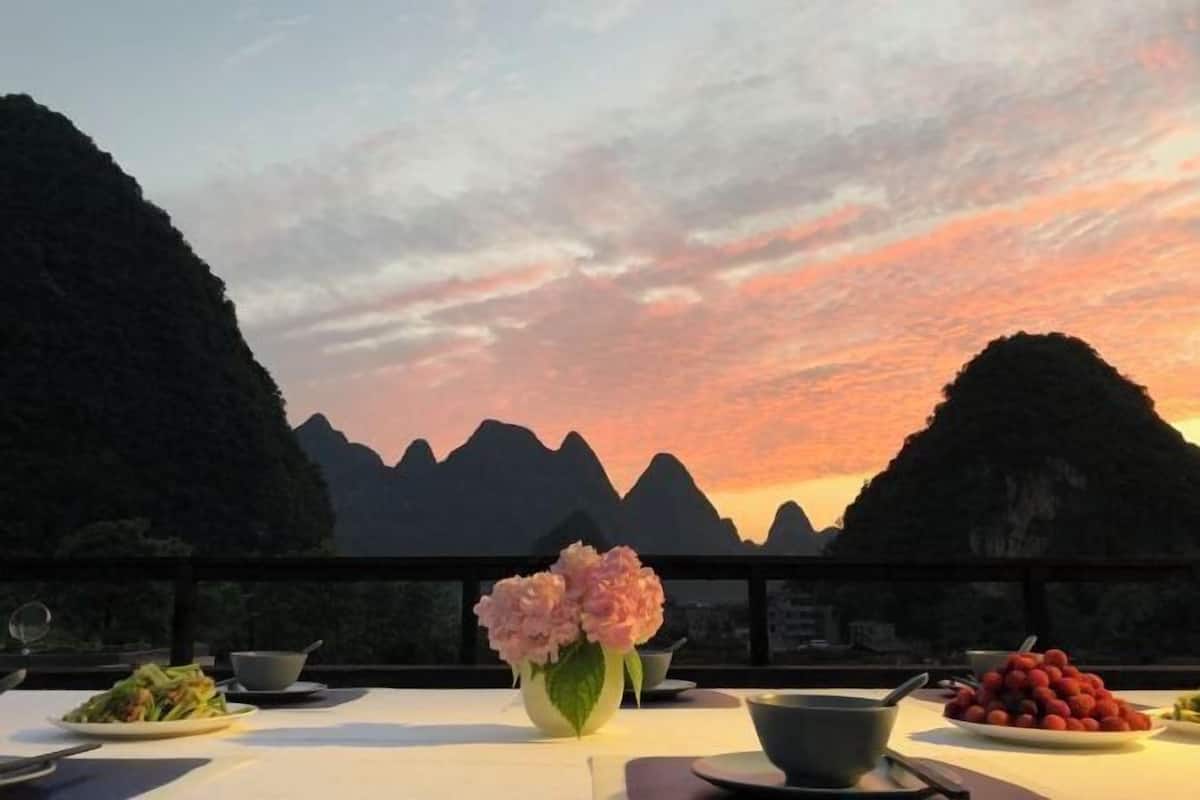 A table set with dishes and a vase of flowers, overlooking a mountainous landscape during sunset.