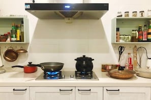 A kitchen with a gas stove, a pot on the burner, a frying pan, and various kitchen utensils. - Zen Box House (Guilin)