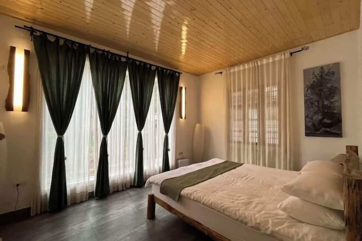 A bedroom with a wooden ceiling, a bed with white bedding, and green curtains.