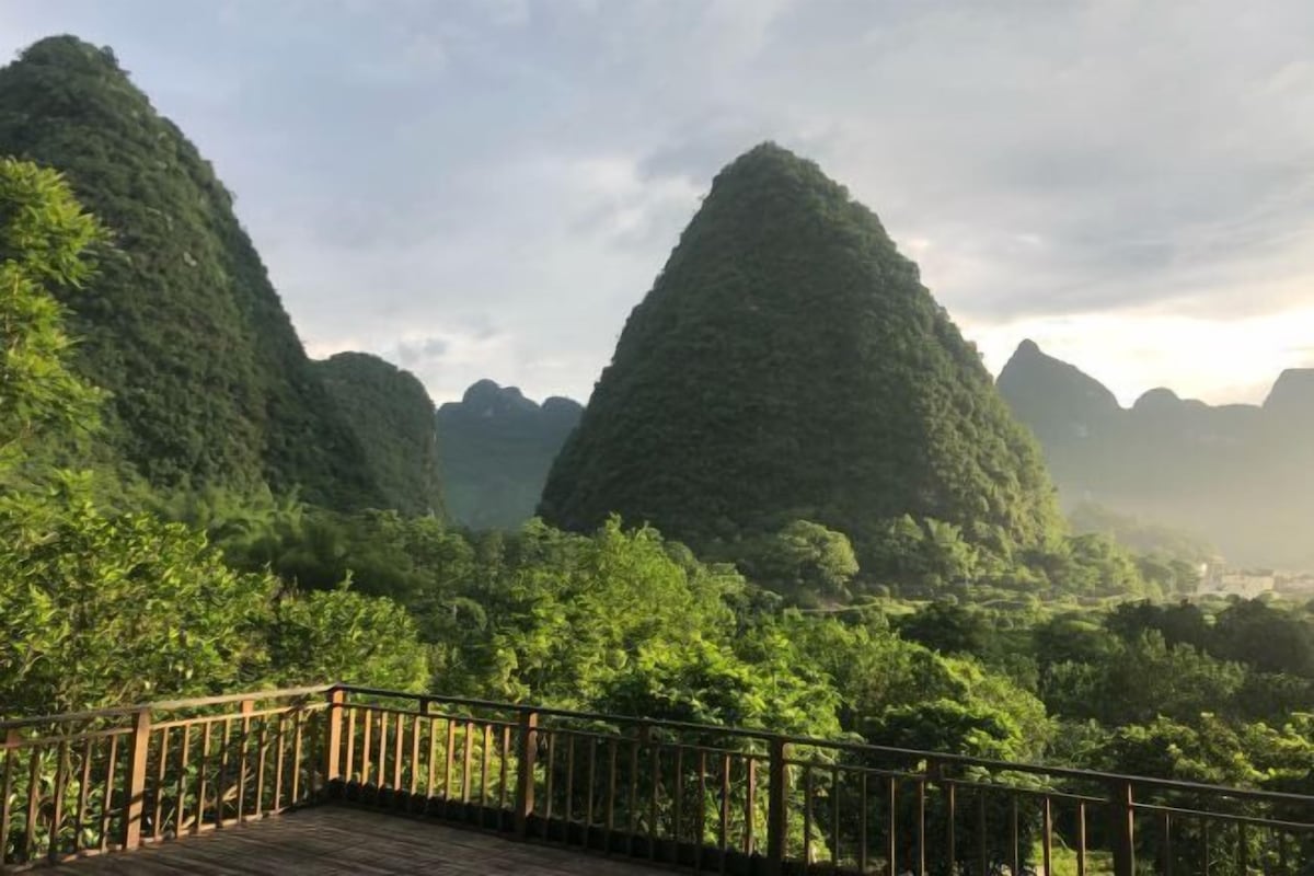A wooden deck with a metal railing overlooking a lush, green landscape with prominent karst limestone hills.
