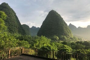 A wooden deck with a metal railing overlooking a lush, green landscape with prominent karst limestone hills. - Zen Box House (Guilin)