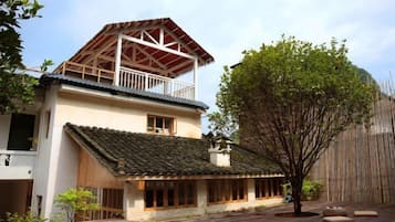 Un edificio de dos pisos con un balcón en el nivel superior, techo de tejas y zona de terraza de madera.