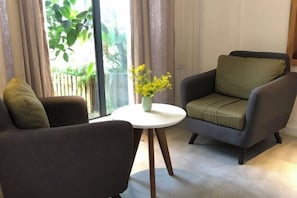 A modern living room with a sofa and armchair, a small round table with a vase of flowers, and a large window with curtains. - Zen Box House (Guilin)