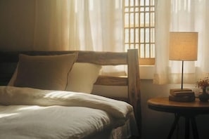 A hotel room with a bed, a nightstand, a lamp, and a window with curtains. - Zen Box House (Guilin)