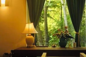 A room with a lamp on a table, a vase with flowers, and a view of greenery through a window. - Zen Box House (Guilin)