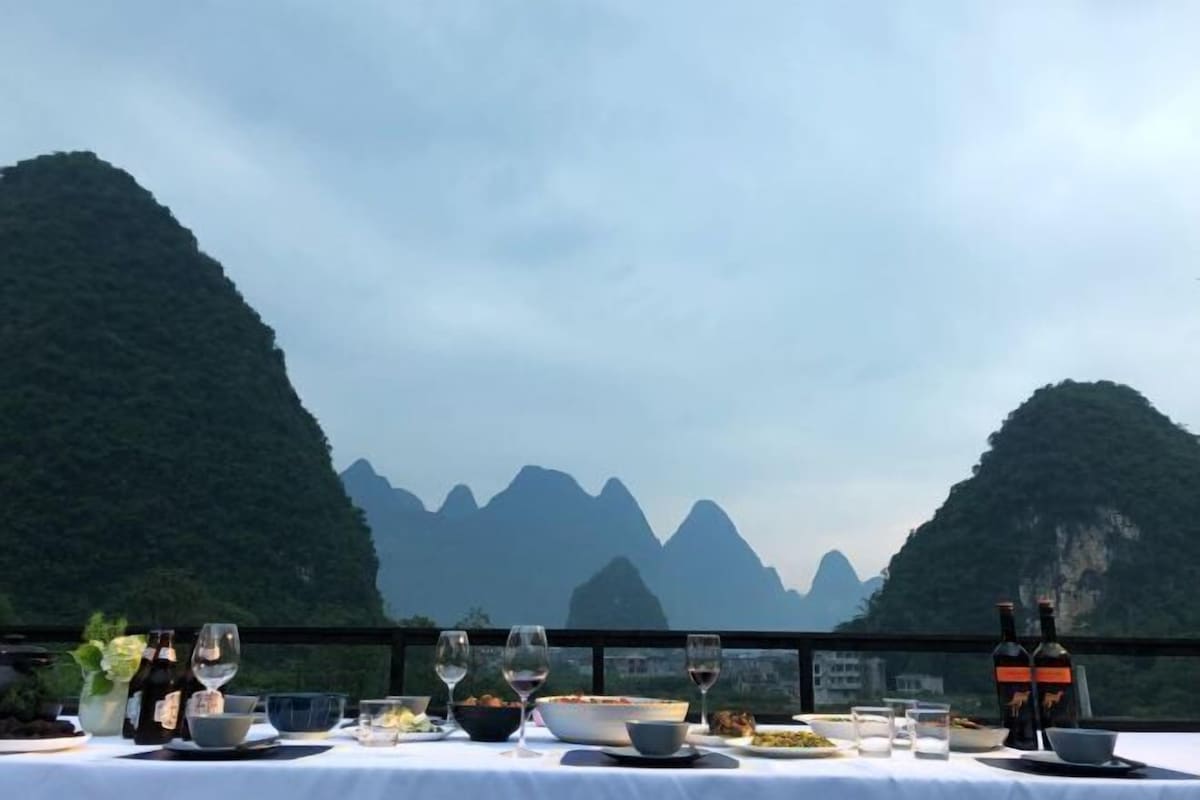 A dining table set with wine glasses, bowls, and bottles, overlooking a mountainous landscape.