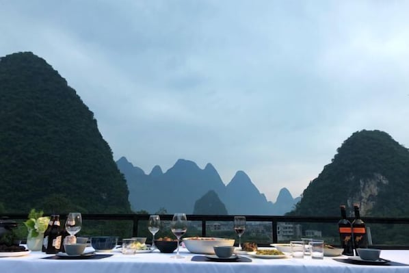 A dining table set with wine glasses, bowls, and bottles, overlooking a mountainous landscape. - Zen Box House (Guilin)