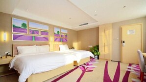 A hotel room with a large bed, a desk, and a chair. There are three wall-mounted artworks depicting landscapes.